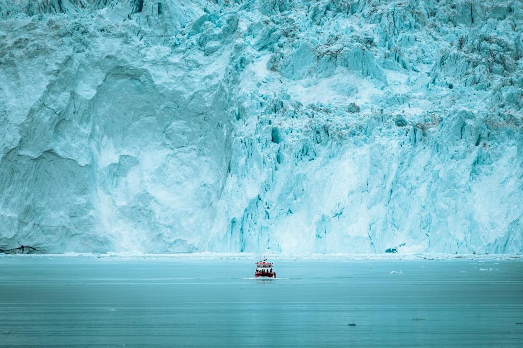 A small passenger boat in front of the huge glacier wall at the Eqi glacier in Greenland