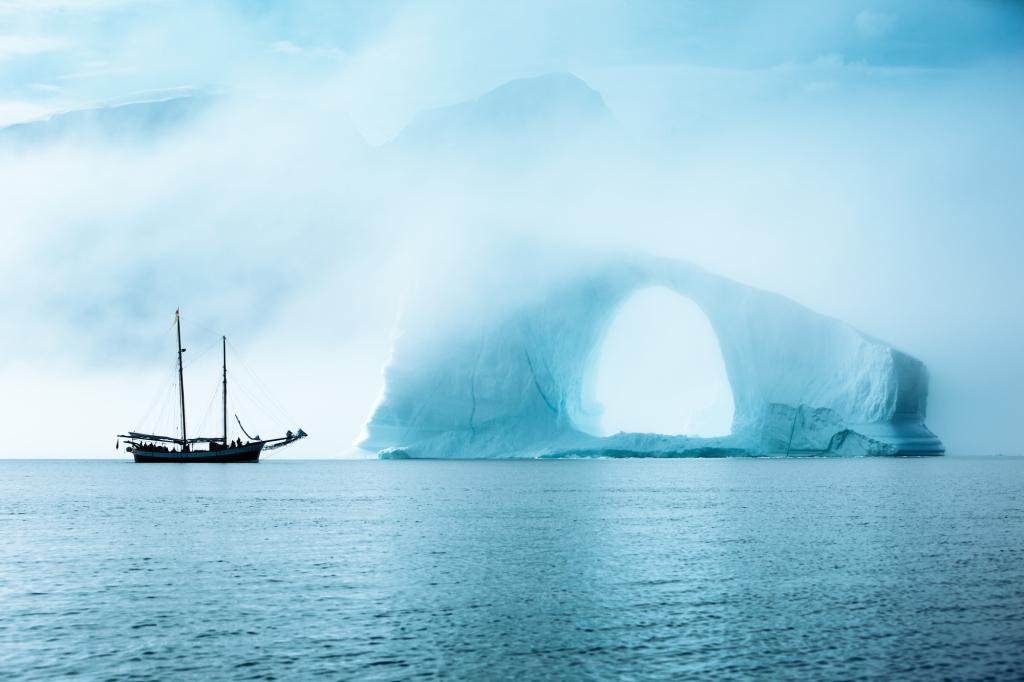 The sailing boat next to an enormous ice arch in Scoresbysund in Greenland